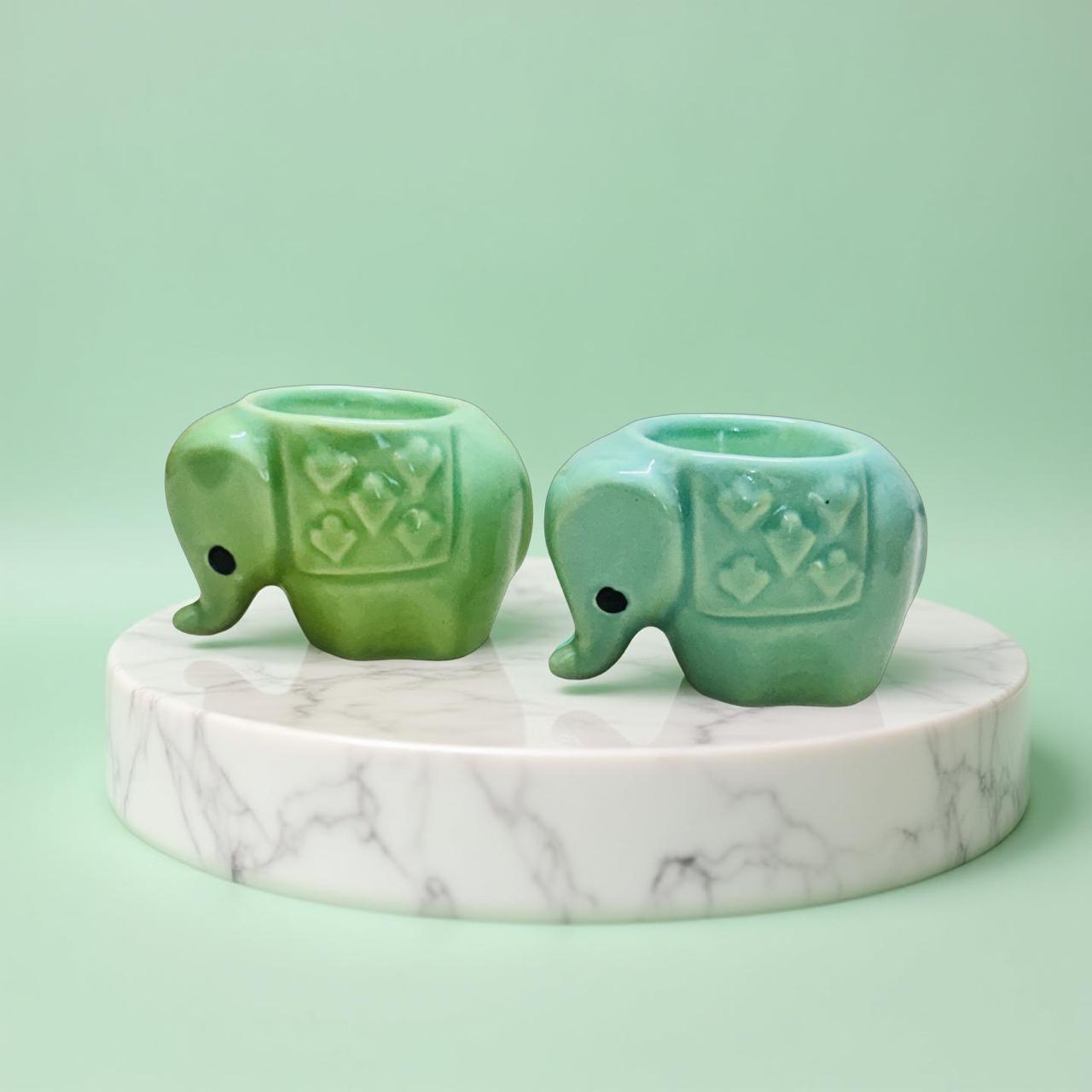 Two green ceramic elephant-shaped candle holders on a marble base against a light green background