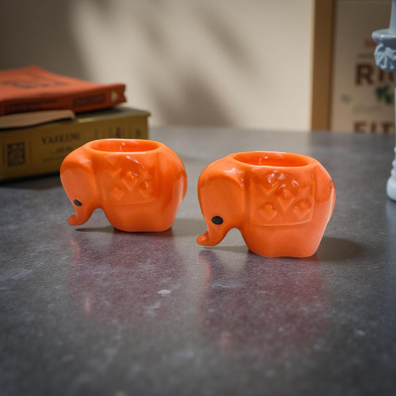 Two orange elephant-shaped objects on a reflective surface with a blurred background.