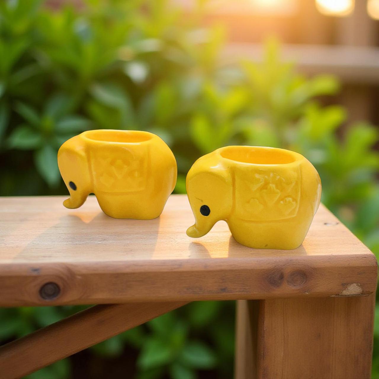 Two yellow elephant-shaped diyas on a wooden surface with a blurred green background