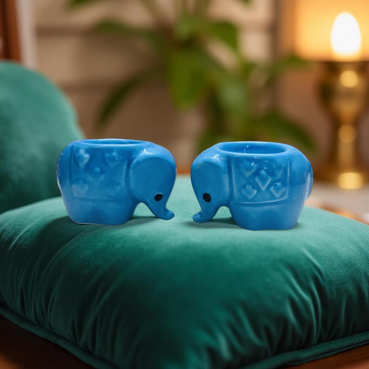 Two blue elephant-shaped candle holders on a green cushion with a blurred background