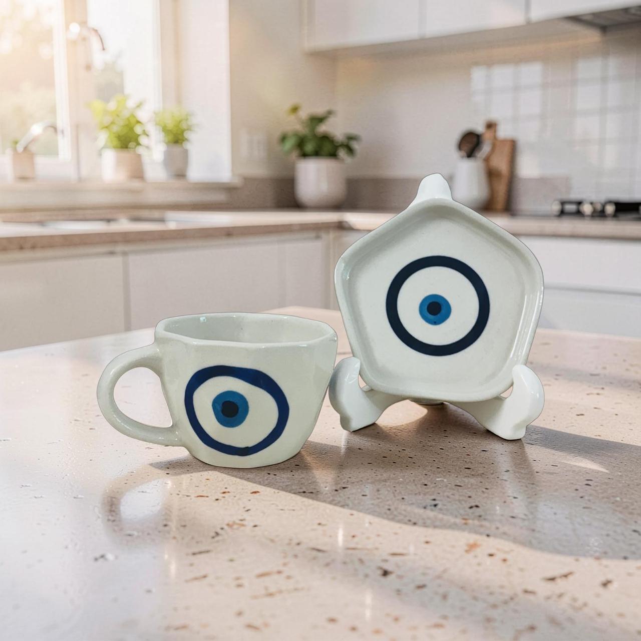 Ceramic cup and decorative dish with blue eye design on a kitchen counter.