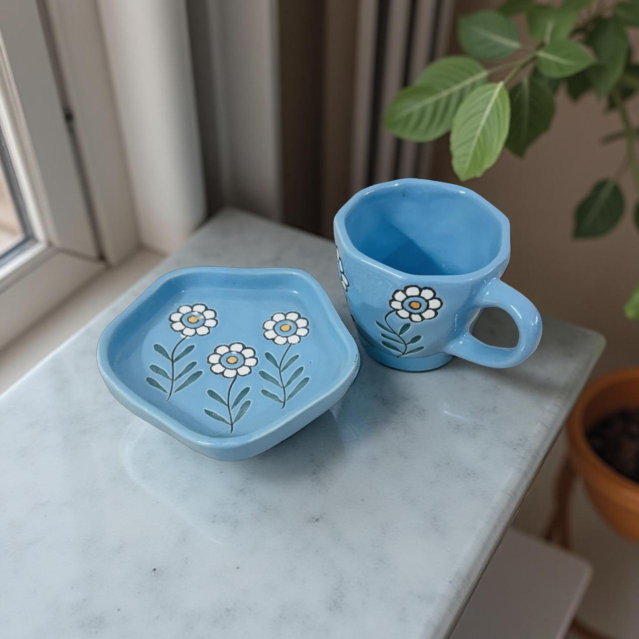 Blue ceramic cup and saucer with floral designs on a marble surface.