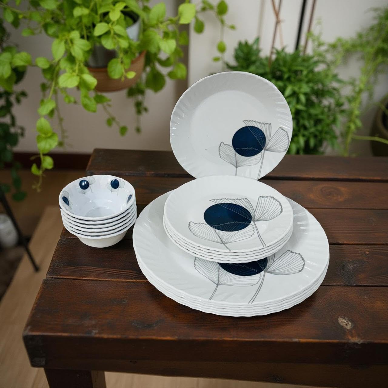 Set of white ceramic plates with blue designs on a wooden table, surrounded by green plants.