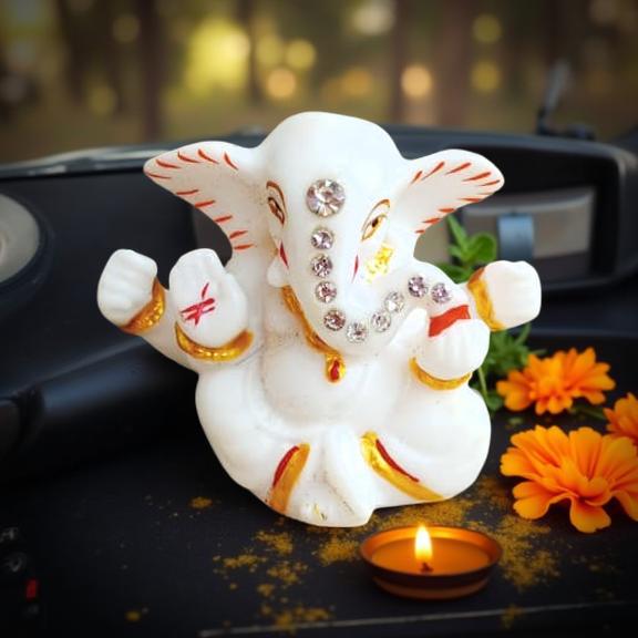 Decorative figure of Ganesha with embellishments on a dark surface with flowers and a candle.
