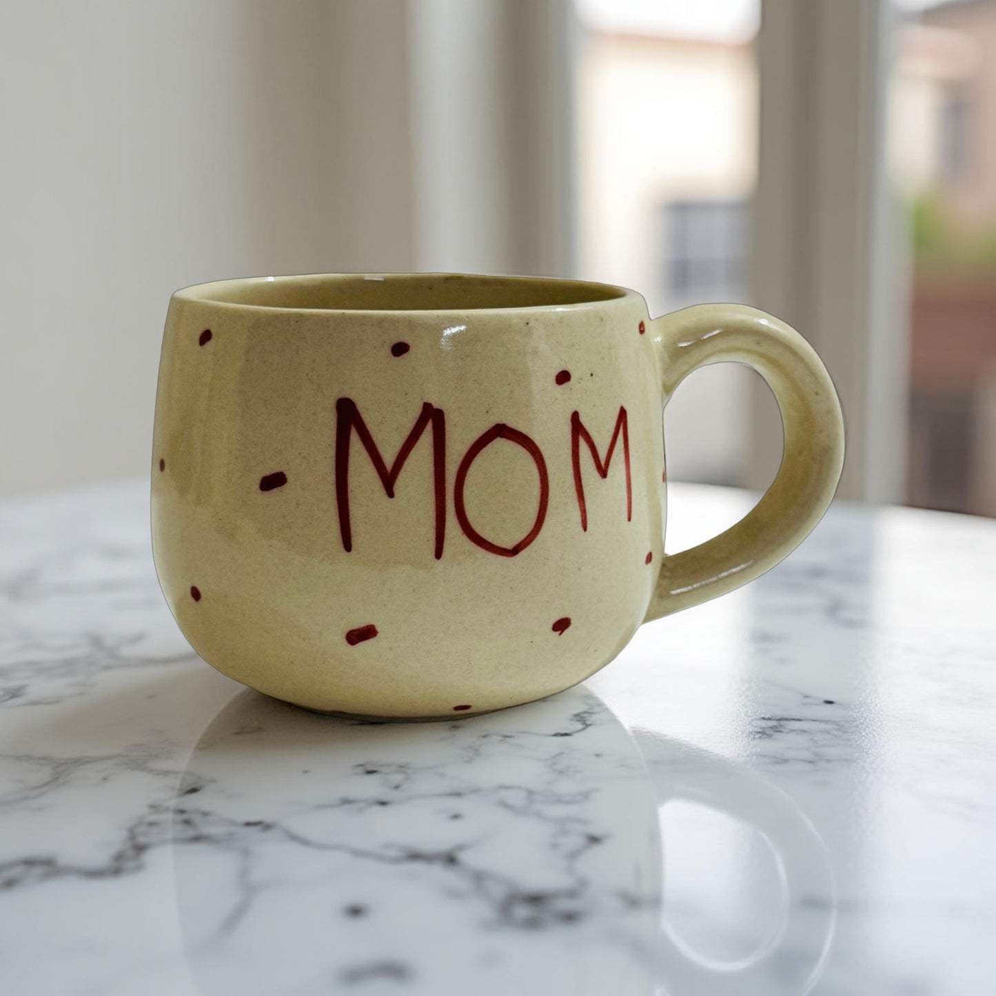 Beige mug with 'MOM' written in red on a marble surface