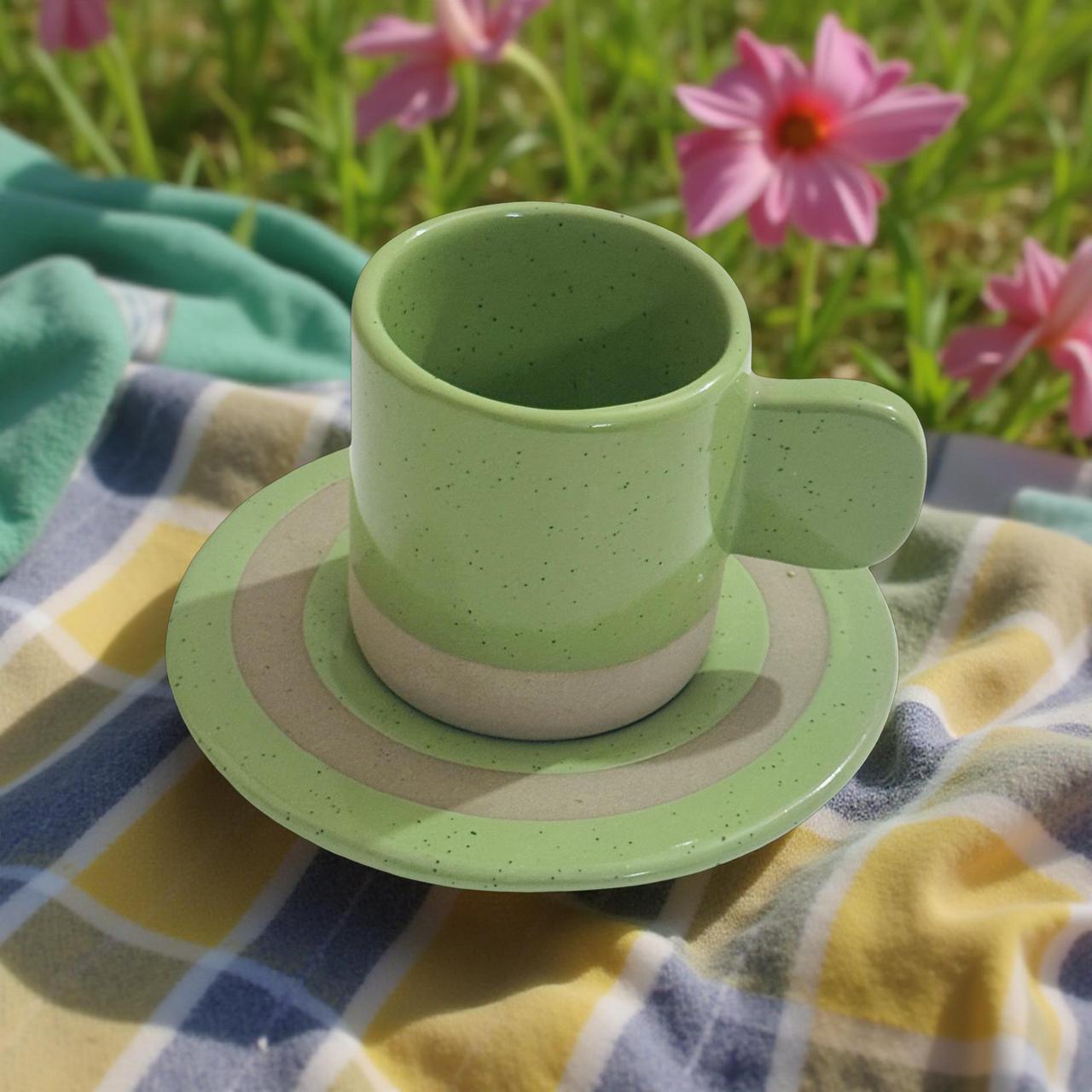 Green ceramic cup and saucer on a checkered blanket with flowers in the background