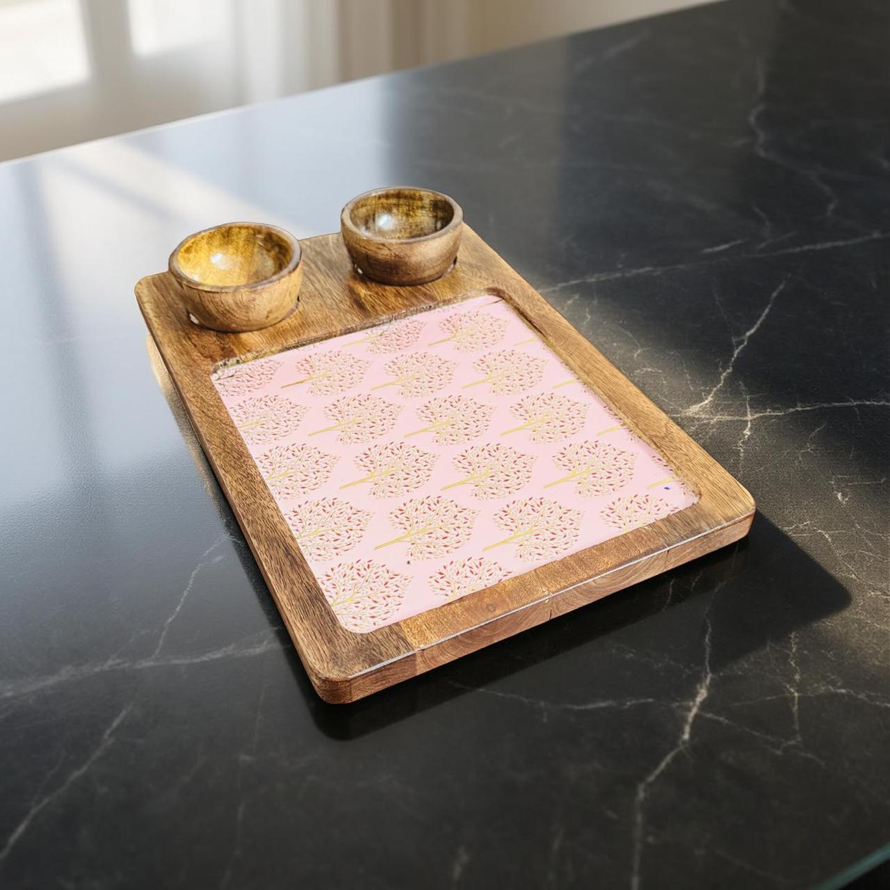 Wooden tray with pink fabric and two small bowls on a dark marble surface