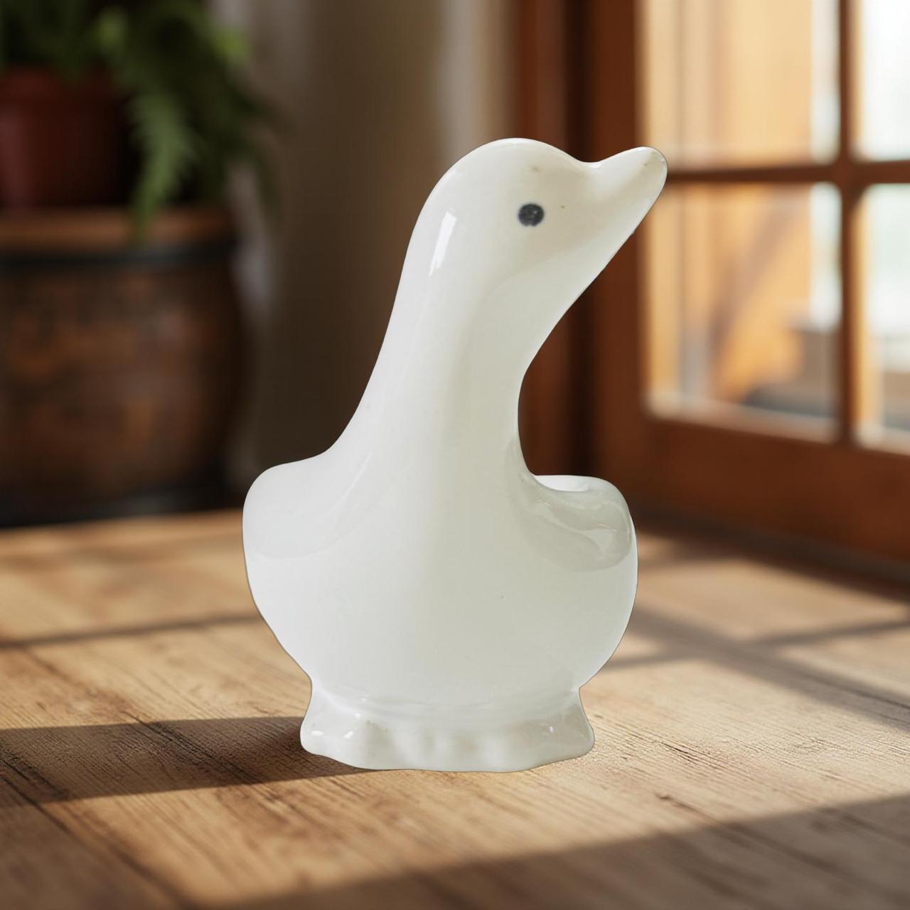 White ceramic goose figurine on a wooden surface with a blurred indoor background
