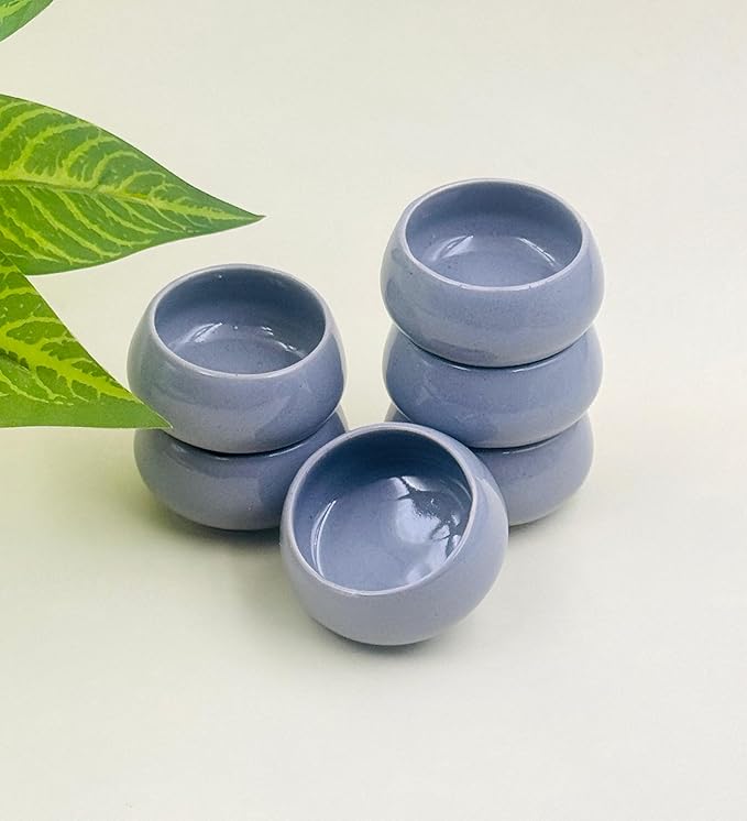 Set of four small blue ceramic bowls stacked on a light background with a green leaf.