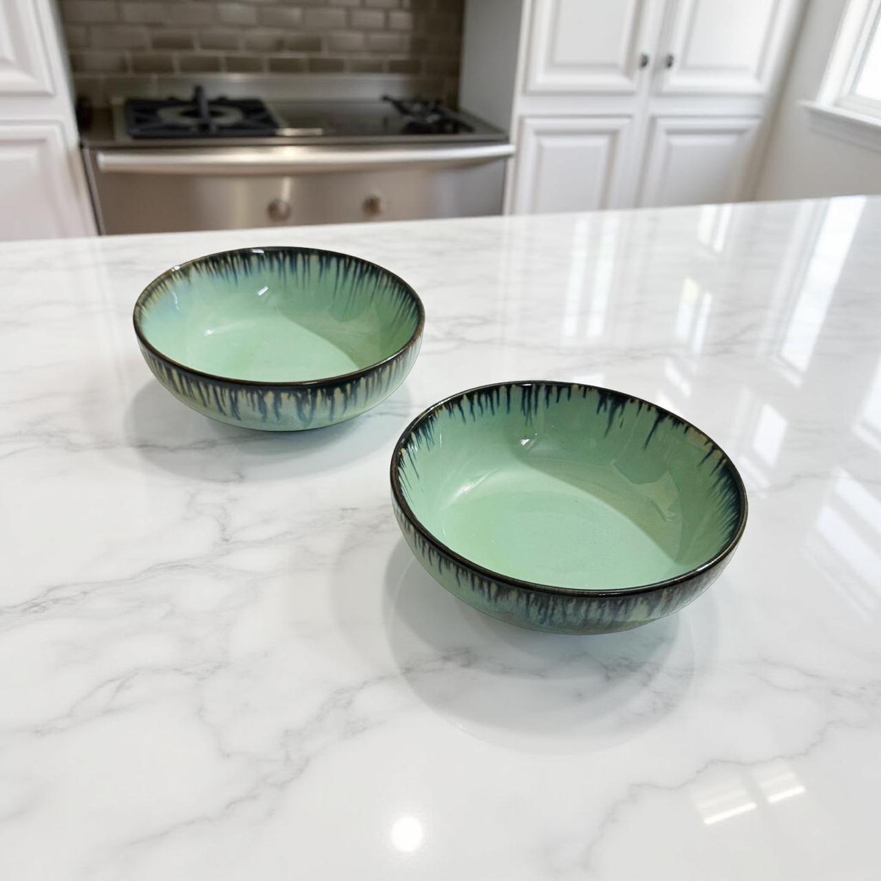 Two green ceramic bowls on a marble countertop with a kitchen background.