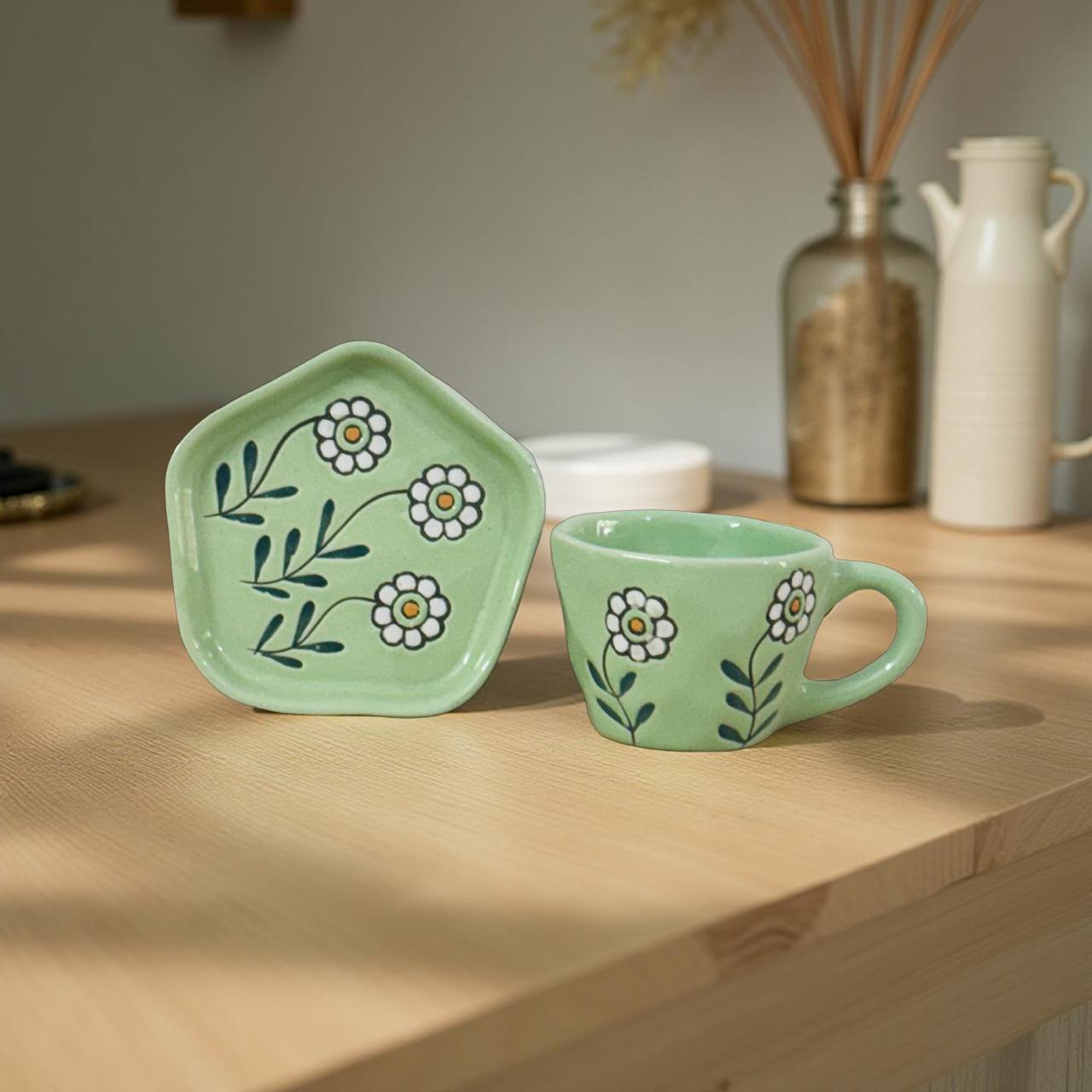 Green ceramic cup and lid with floral design on a wooden surface