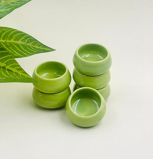 Stack of green ceramic bowls on a light background with a leaf decoration.