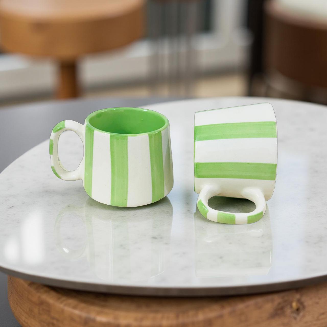 Two green and white striped ceramic mugs on a marble surface.