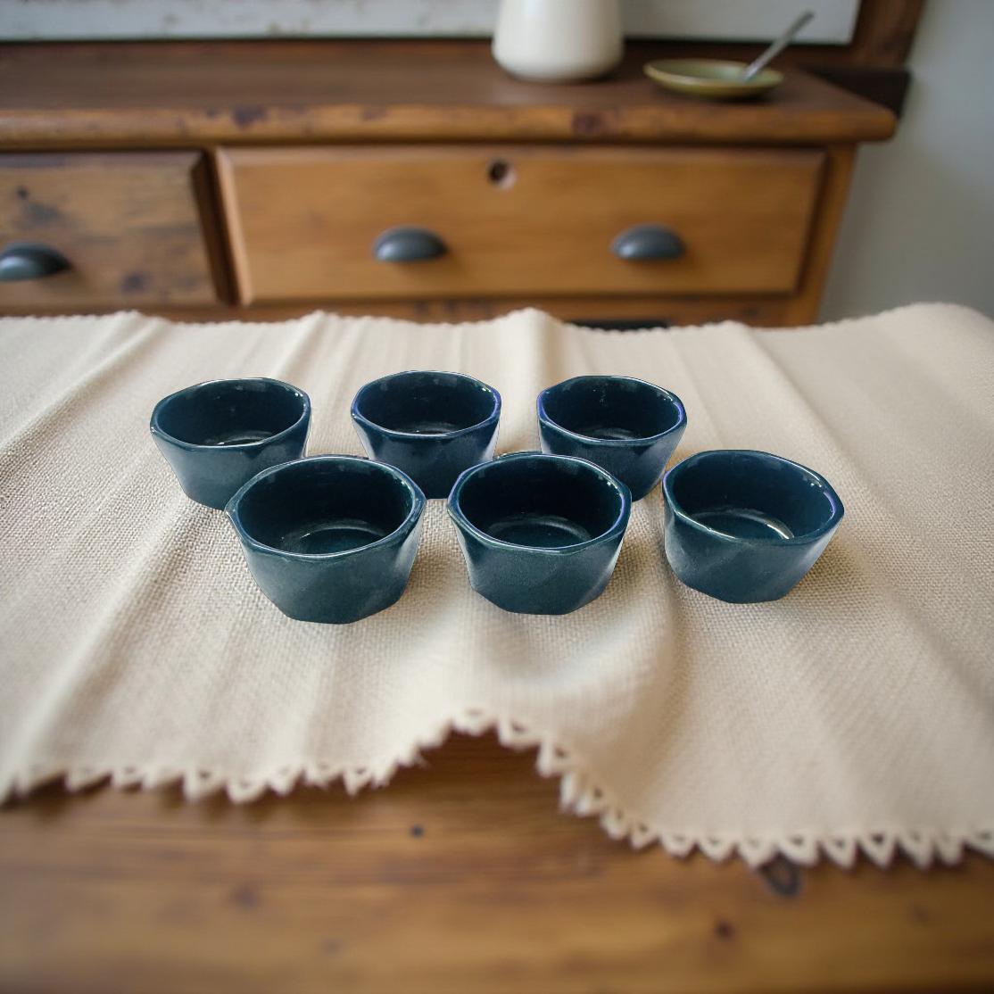 Set of six blue ceramic cups on a beige cloth with a wooden drawer in the background.