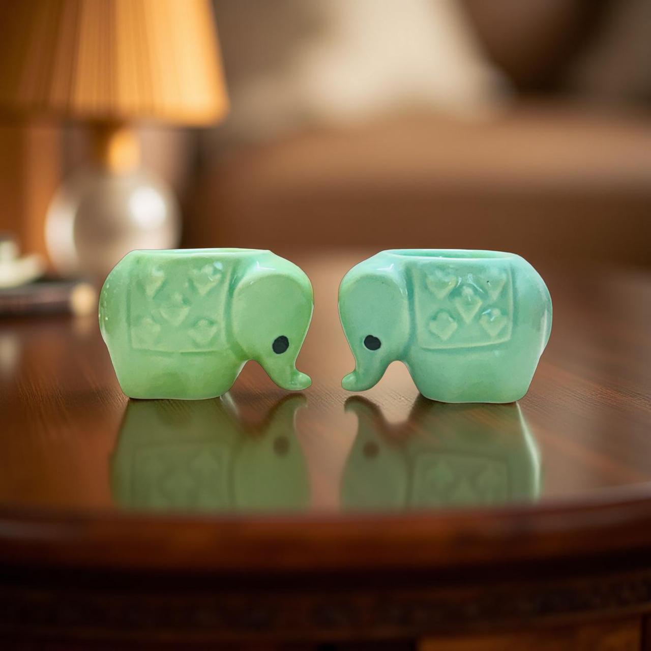 Two green elephant-shaped objects on a reflective surface with a blurred background
