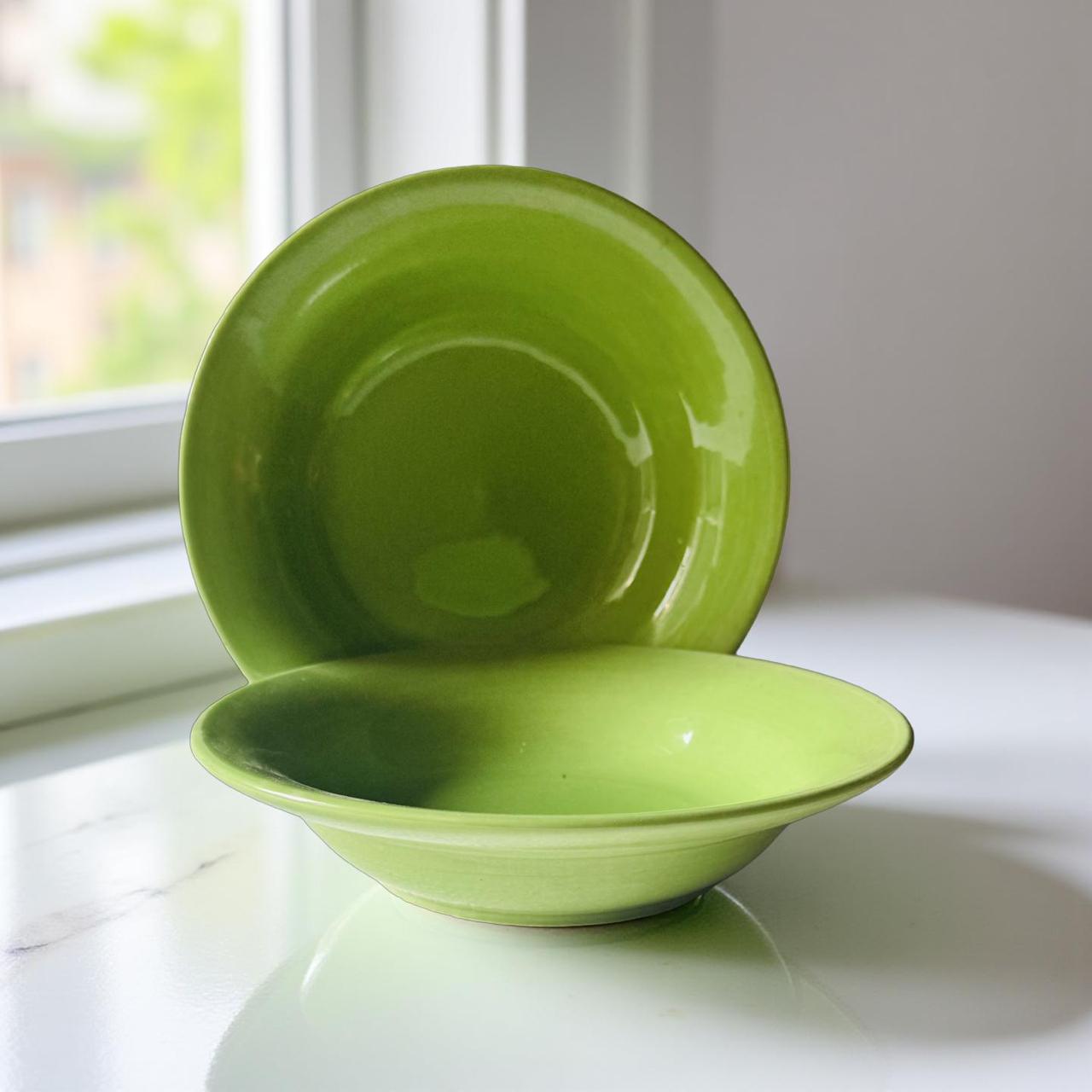Two green ceramic bowls on a white surface with a blurred window background