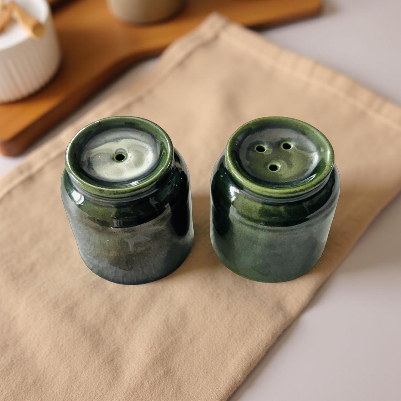 Two green ceramic salt and pepper shakers on a beige cloth with a wooden surface in the background.