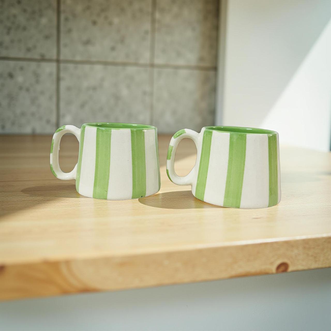 Two green and white striped mugs on a wooden surface with a tiled wall background.