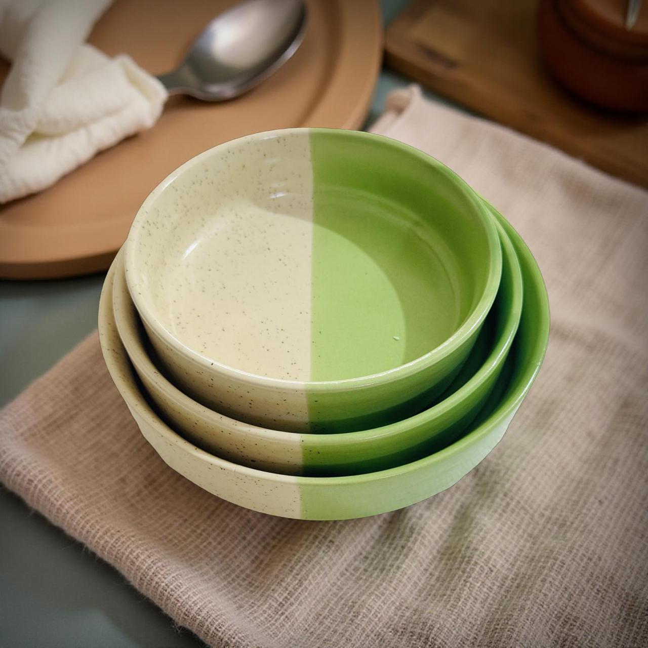 Stack of green ceramic bowls on a textured surface with a spoon in the background.