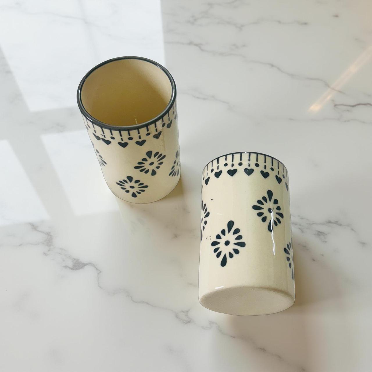 Two ceramic cups with black floral patterns on a marble surface