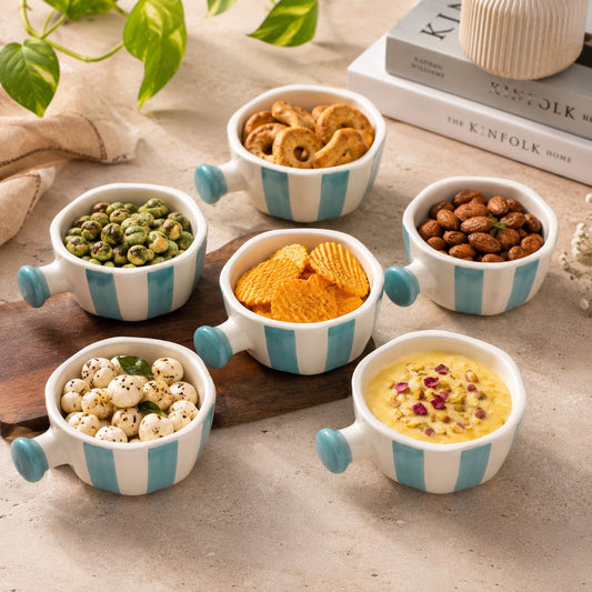 Set of small bowls with striped handles, each containing different snacks on a wooden surface.