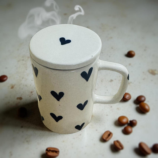 White mug with black heart patterns on a light surface with coffee beans and steam.
