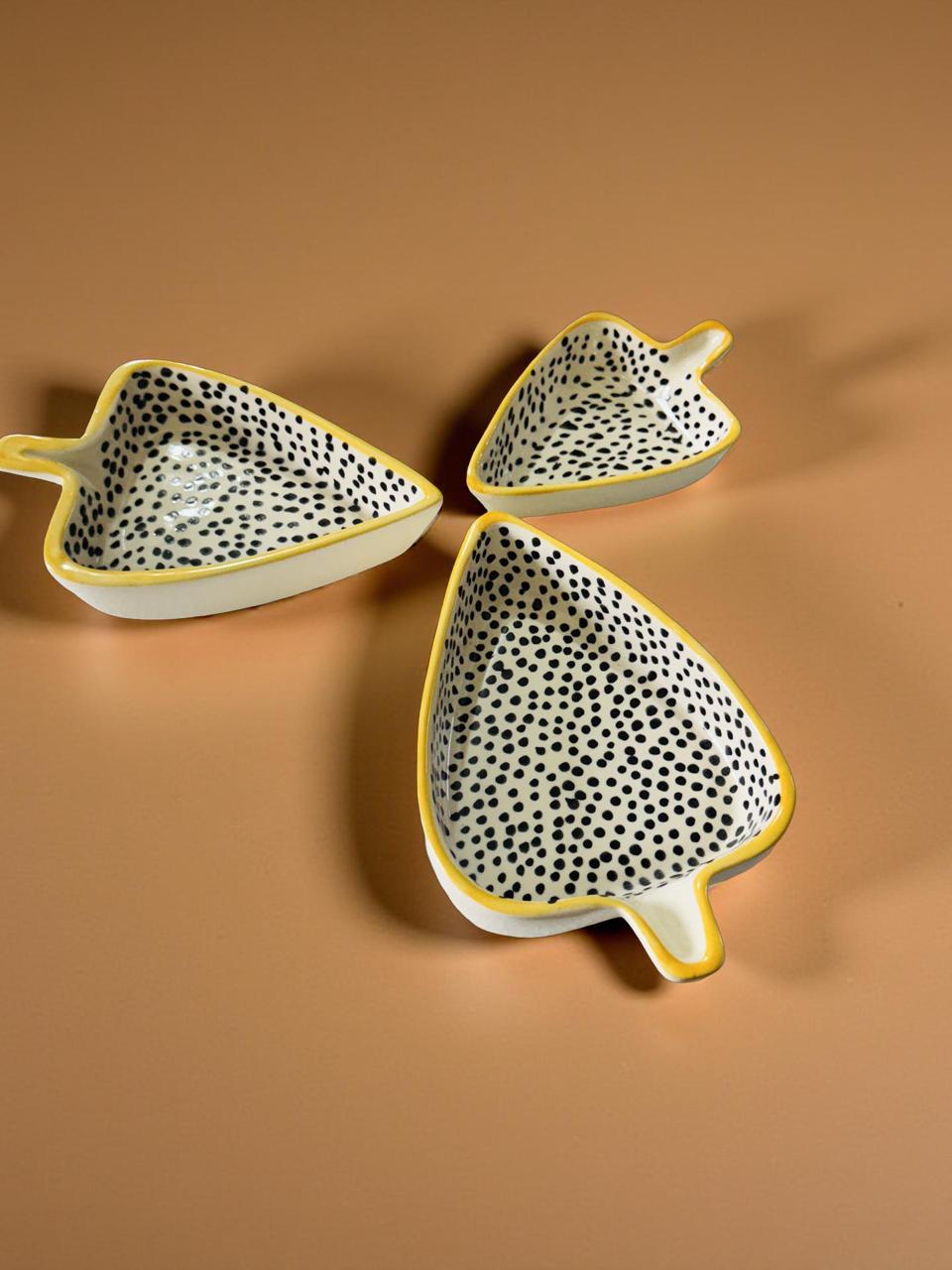 Three ceramic leaf-shaped dishes with black dot patterns on a brown background