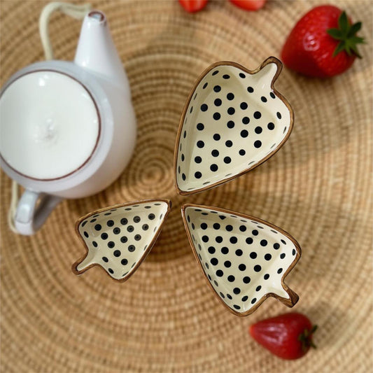 Three leaf-shaped ceramic snack serving set on a woven mat with strawberries and a teapot.