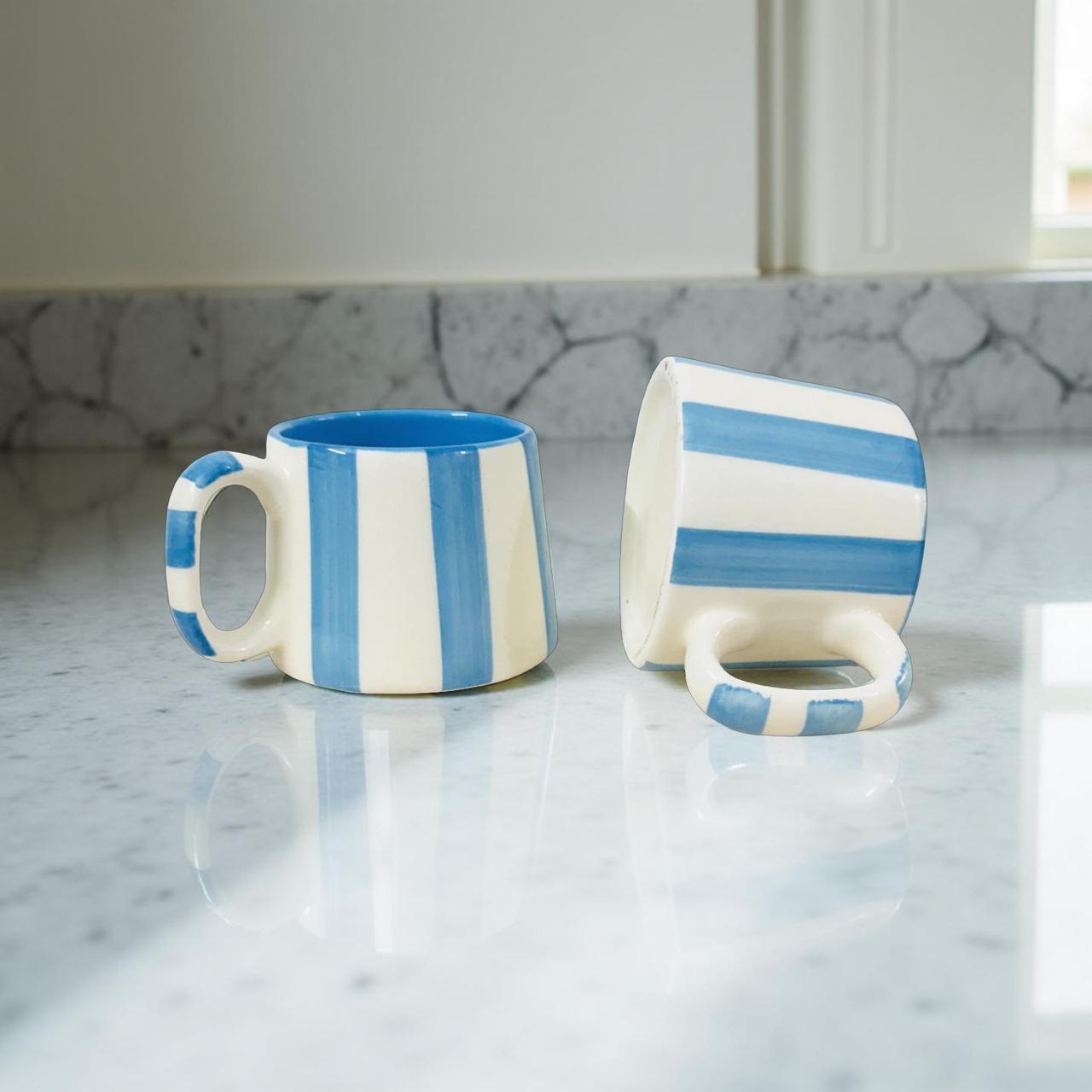 Two blue and white striped ceramic mugs on a marble surface.