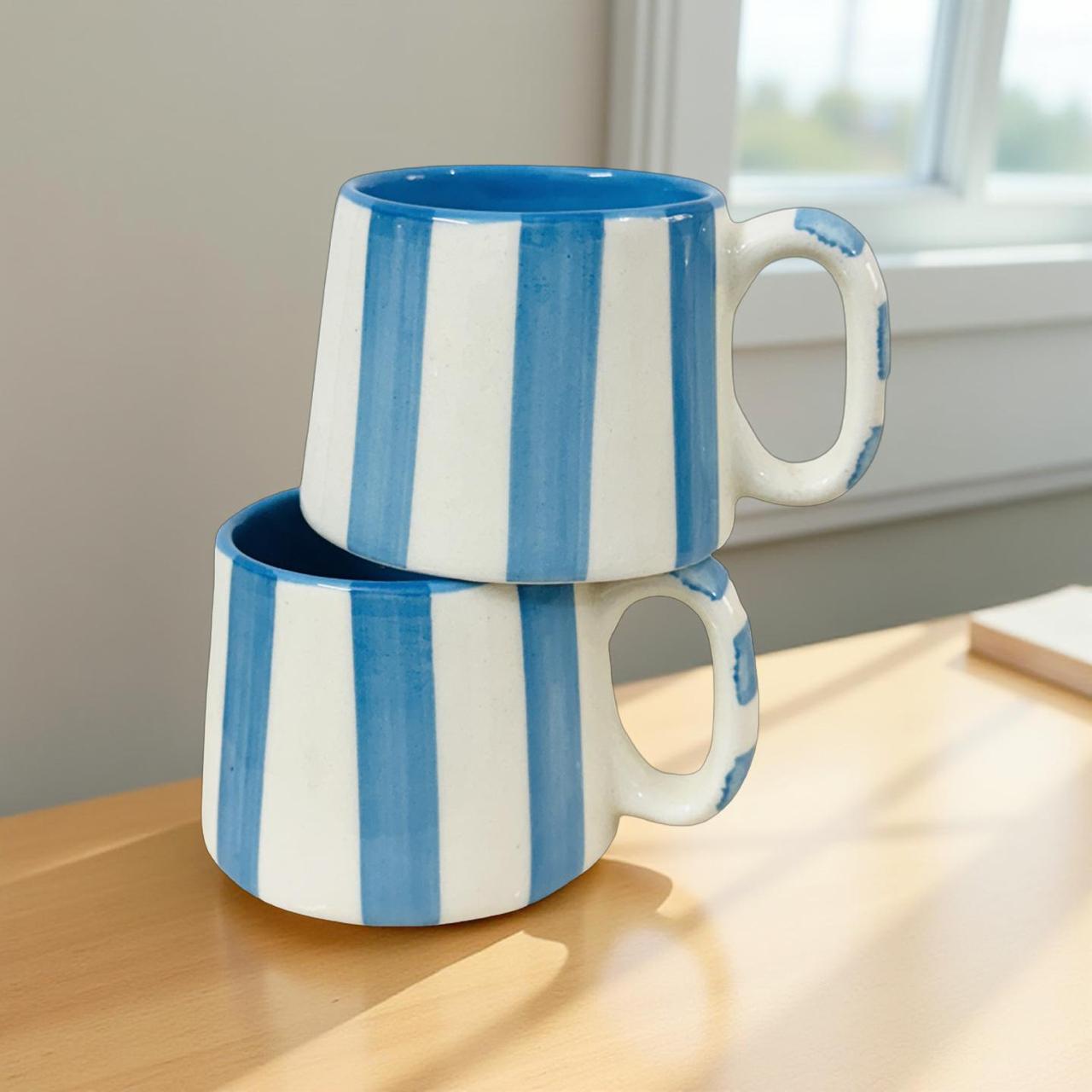Two blue and white striped mugs stacked on a wooden surface with a neutral background.