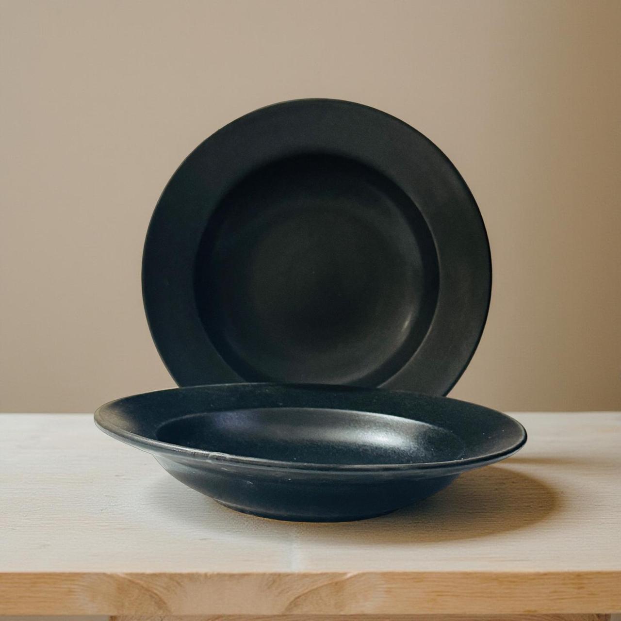 Two black ceramic pasta bowls on a wooden surface with a beige background