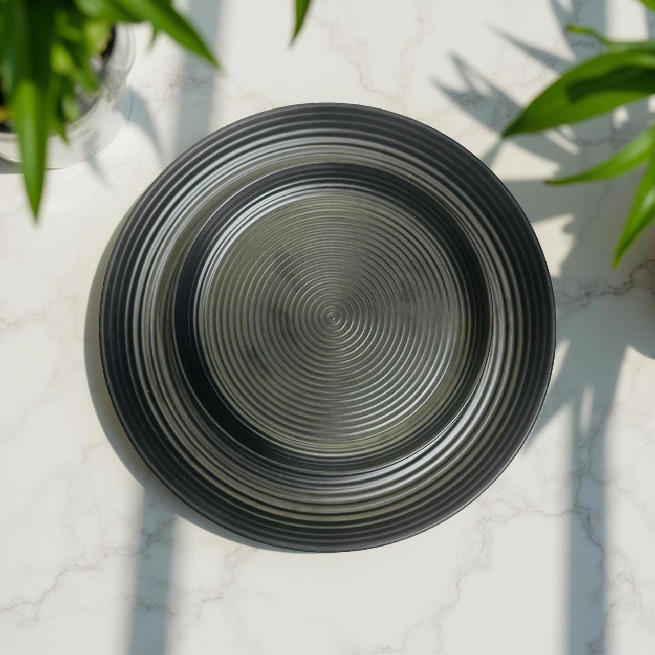 Black melamine plate with concentric circular design on a light gray surface with green leaves.