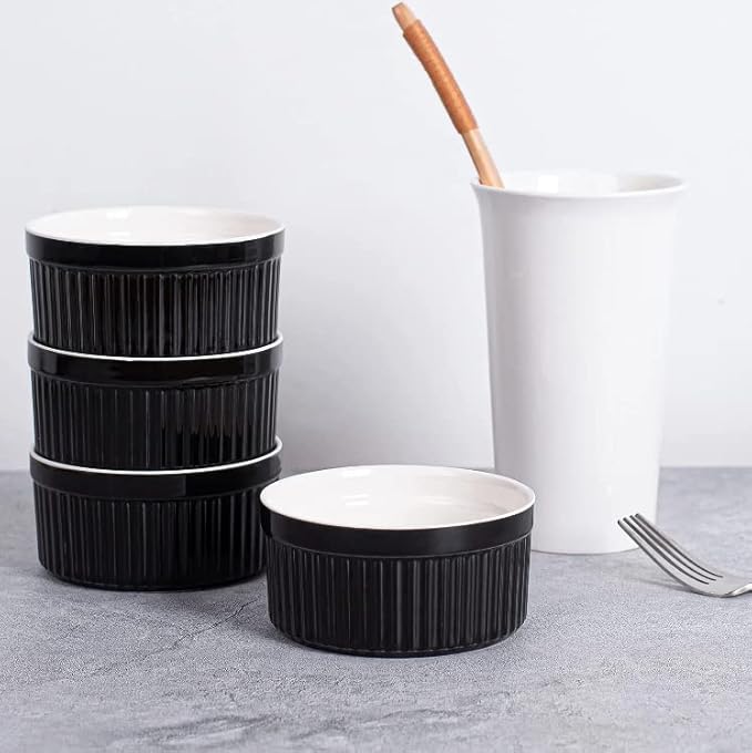 Set of black ceramic bowls on a gray surface with a white mug and wooden spoon in the background.