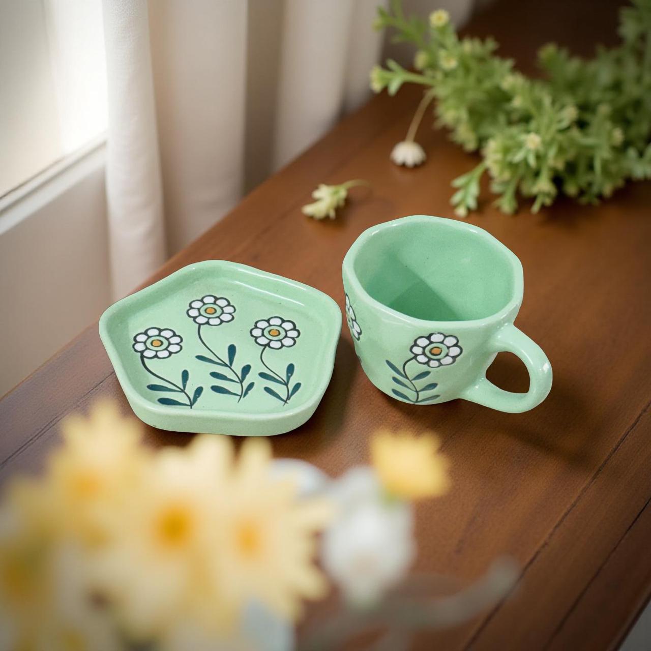 Green ceramic mug and tray with floral design on a wooden surface.