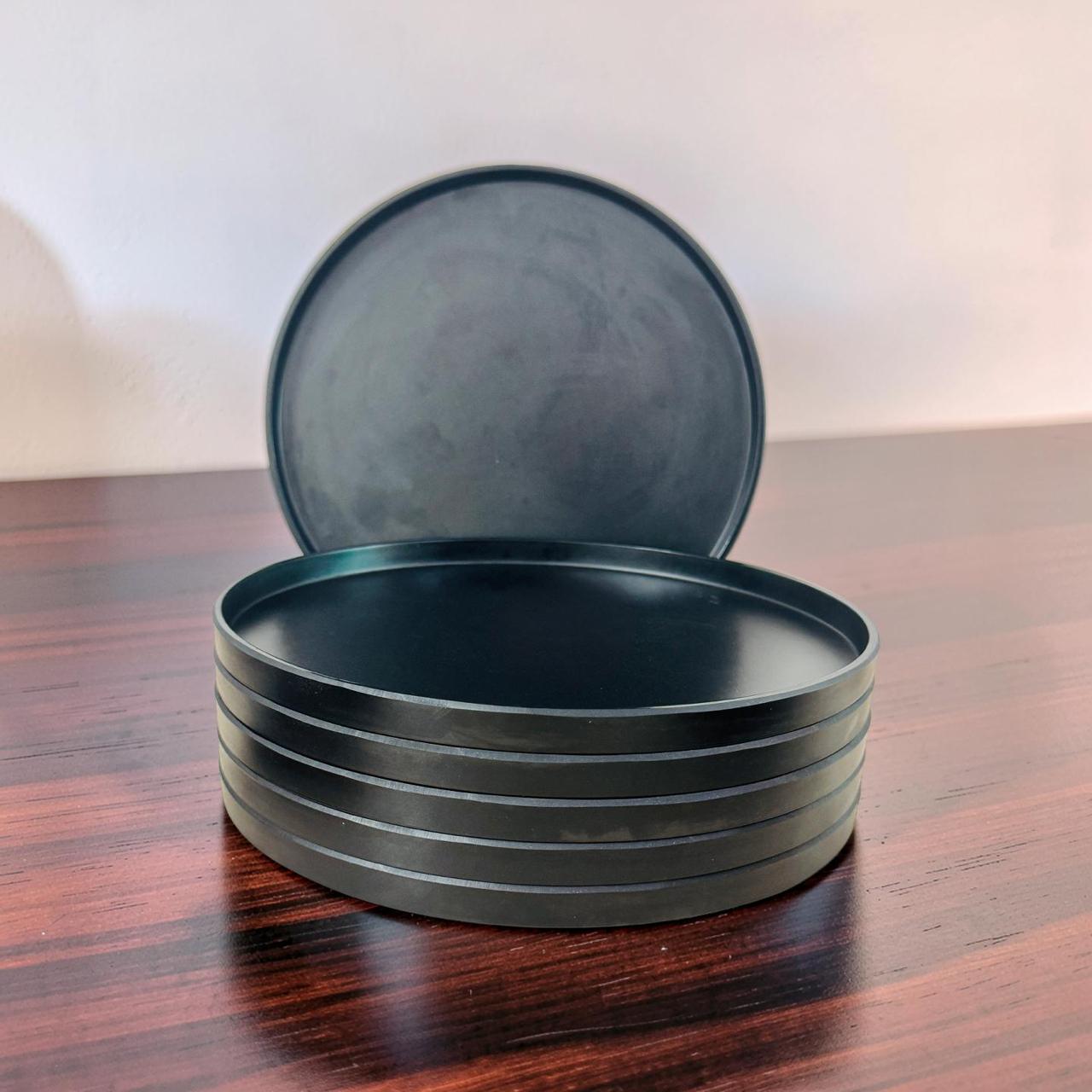 Stack of black ceramic plates on a wooden surface with a white background
