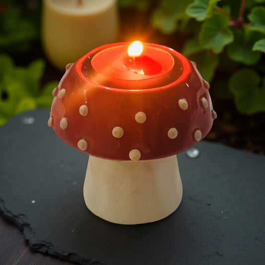 Mushroom-shaped candle holder with a lit candle on a dark surface with greenery in the background