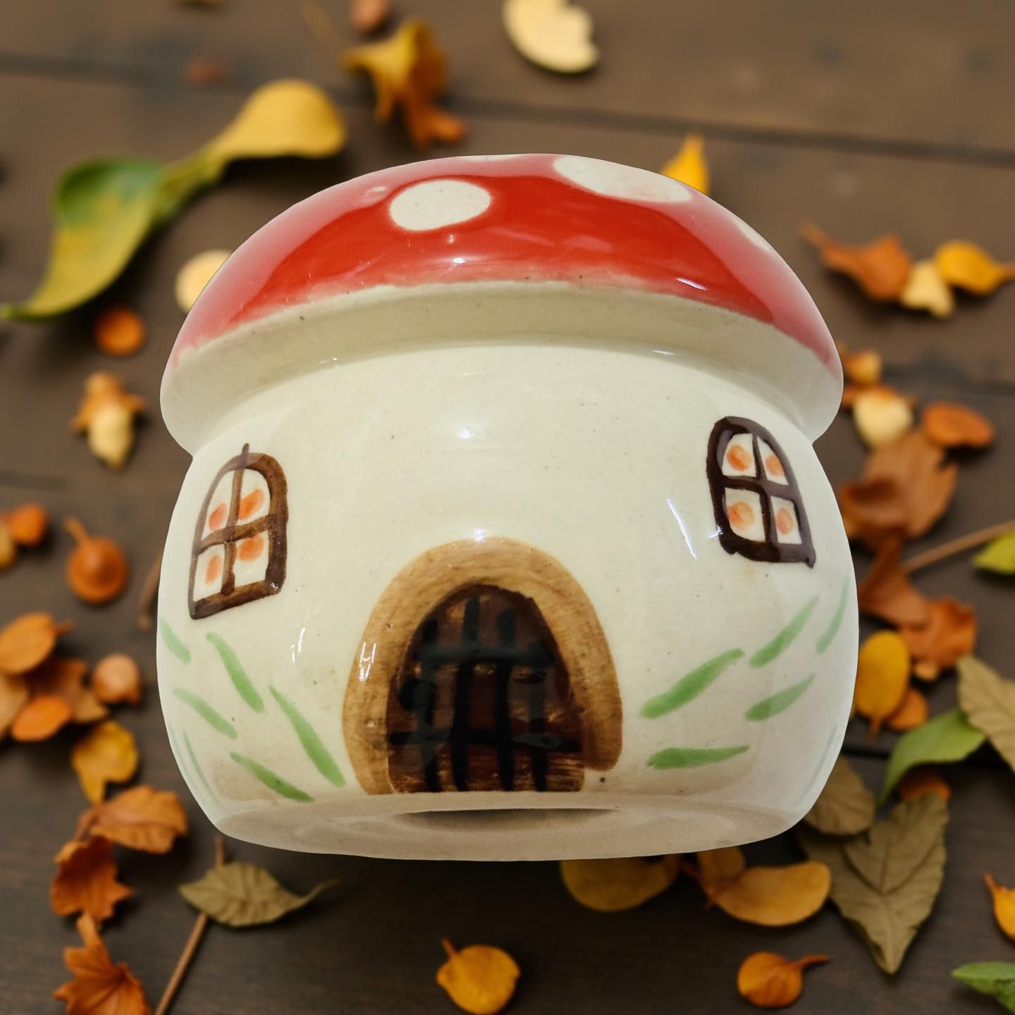 Ceramic mushroom-shaped house with red cap and white body on a surface with autumn leaves.