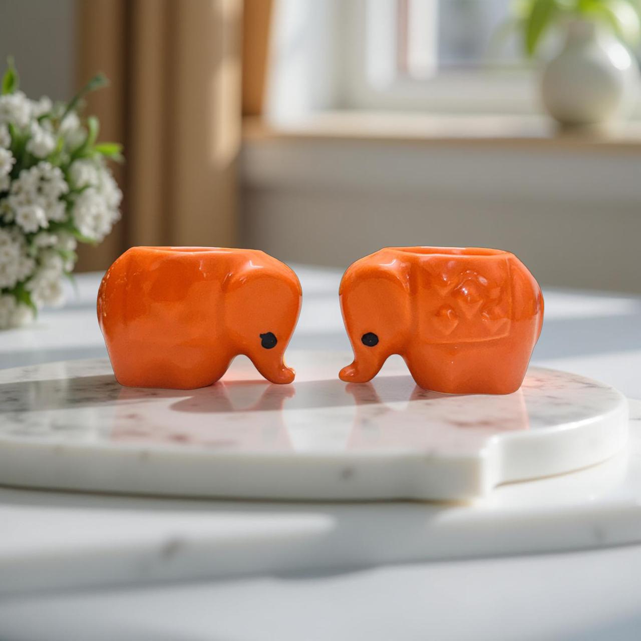 Two orange elephant-shaped objects on a marble surface with a blurred indoor background.