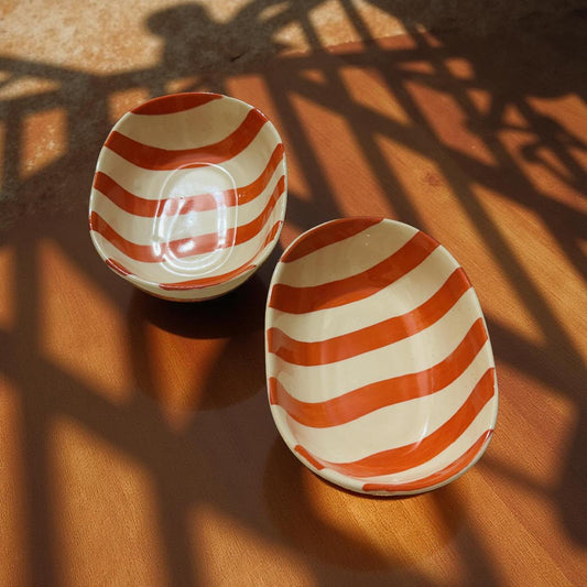 Two ceramic bowls with red and white striped pattern on a wooden surface.