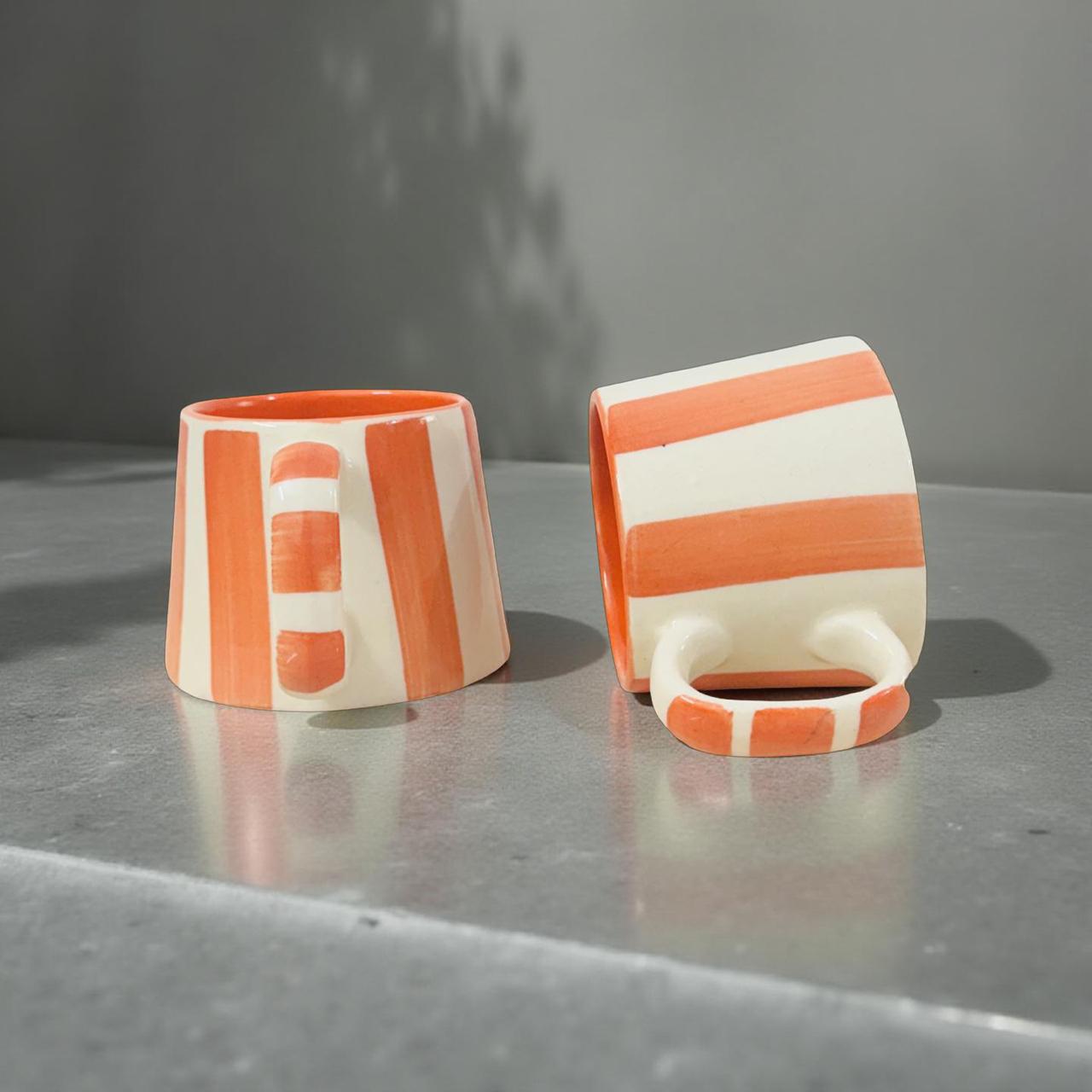 Two ceramic cups with orange and white stripes on a gray surface.
