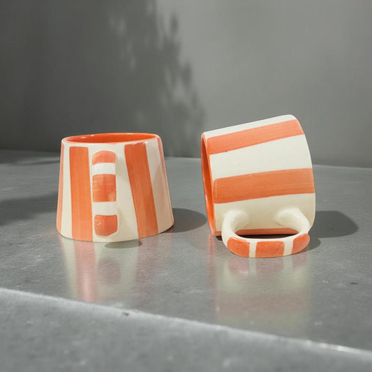 Two ceramic cups with orange and white stripes on a gray surface.