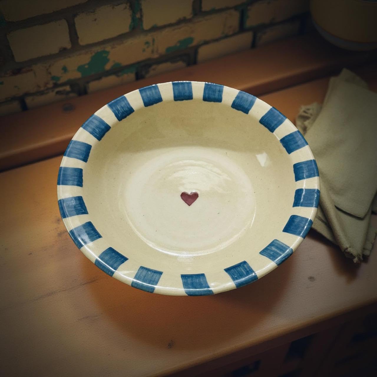 Ceramic bowl with blue striped rim and heart design on a wooden surface.