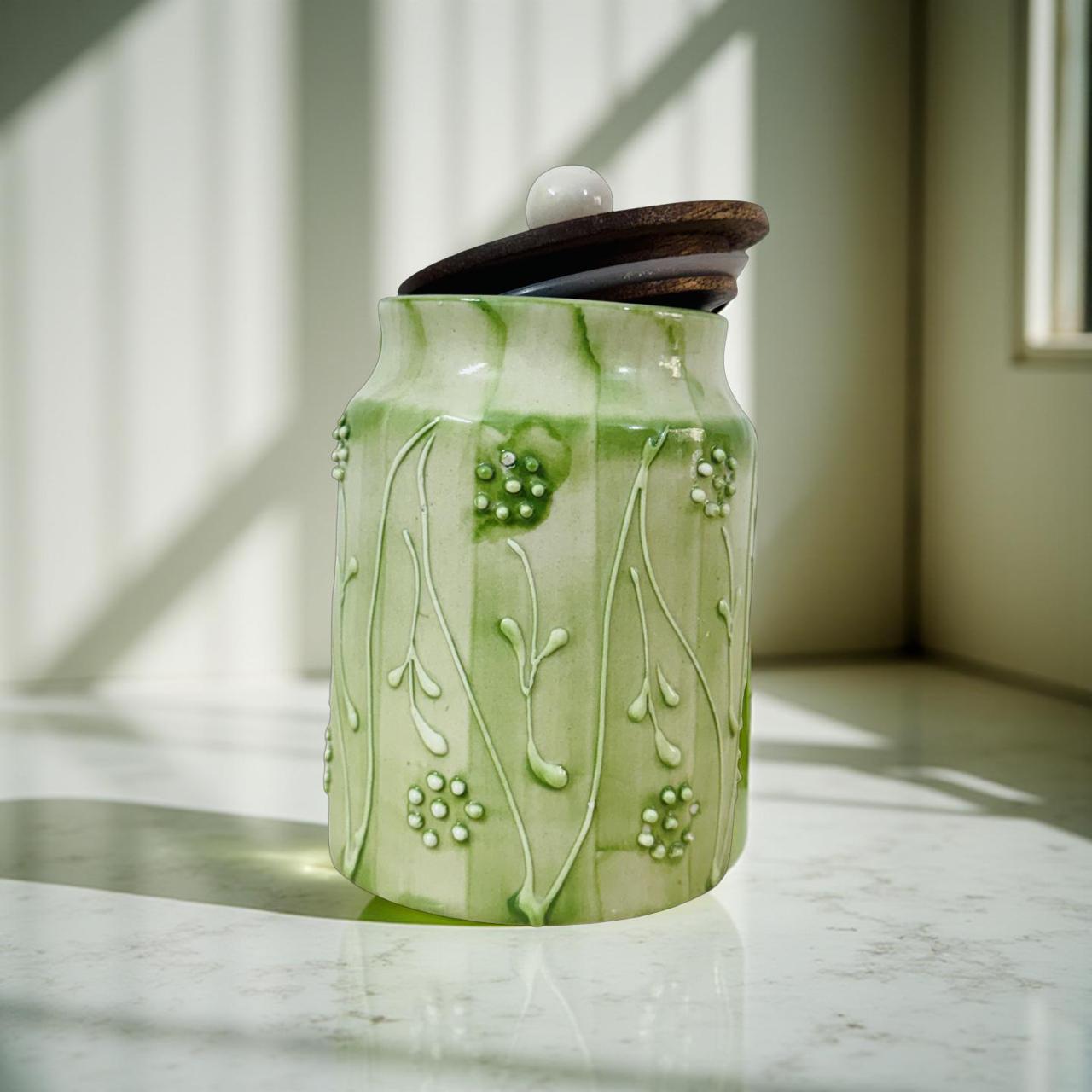 Green ceramic jar with floral patterns on a marble surface