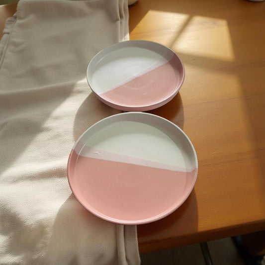 Two pink and white ceramic plates on a wooden surface with a light fabric background.