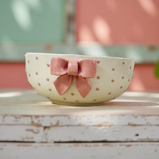 Ceramic bowl with pink polka dots and a matching bow on a wooden surface.