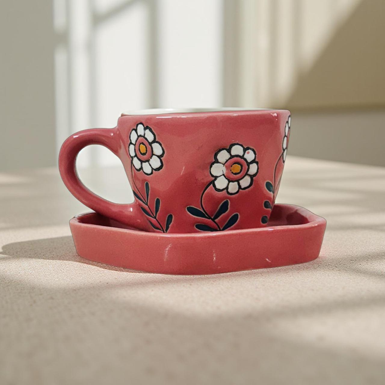 Pink ceramic cup with hand‑painted daisy floral design and matching saucer