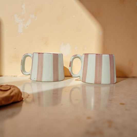 Two striped ceramic mugs on a reflective surface with a beige background