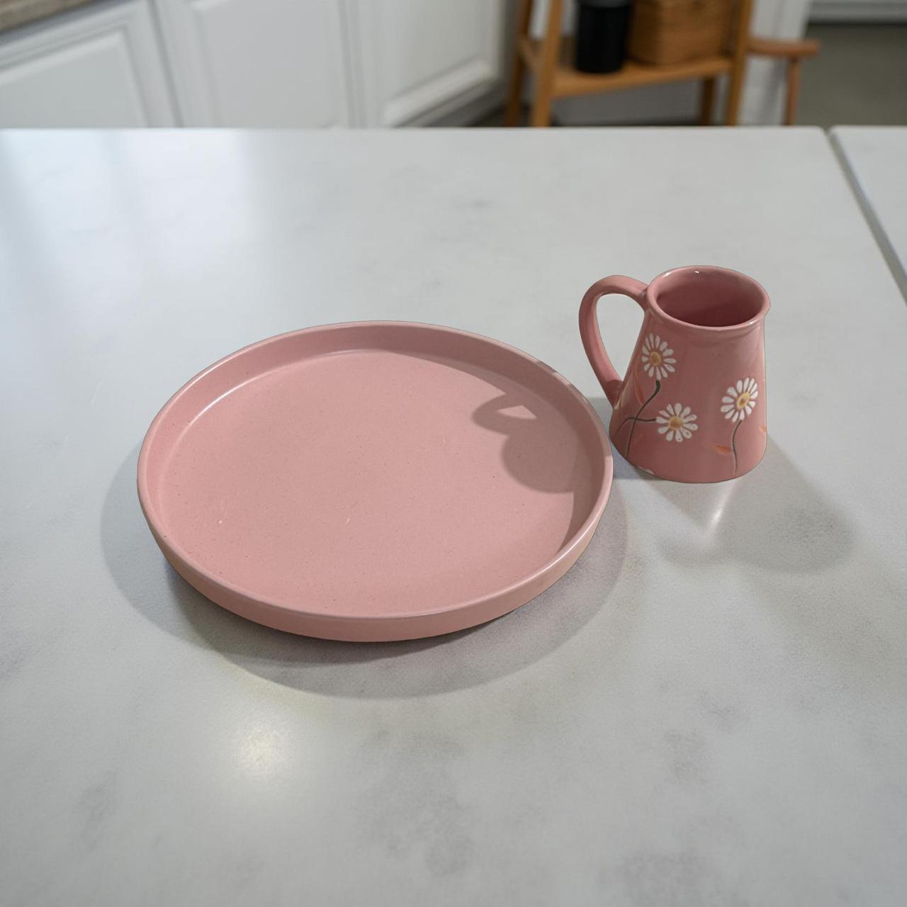 Pink ceramic plate and mug with floral design on a white surface