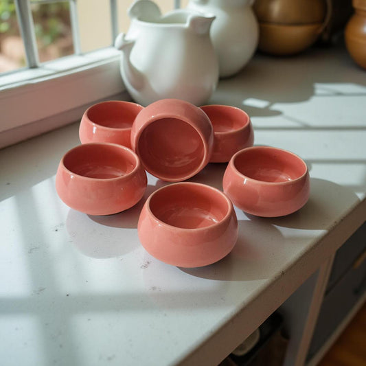 Set of six pink ceramic bowls on a light surface with a blurred background