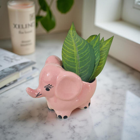 Pink elephant-shaped planter with a green plant on a marble surface